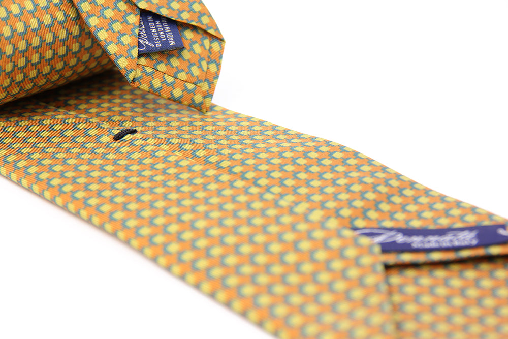 A patterned silk tie with a combination of ochre and blue colors, displayed in a folded and unfolded configuration.