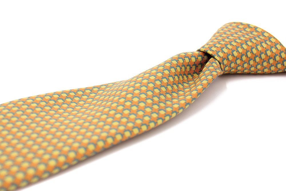 A patterned silk tie with a combination of ochre and blue colors, displayed in a folded and unfolded configuration.