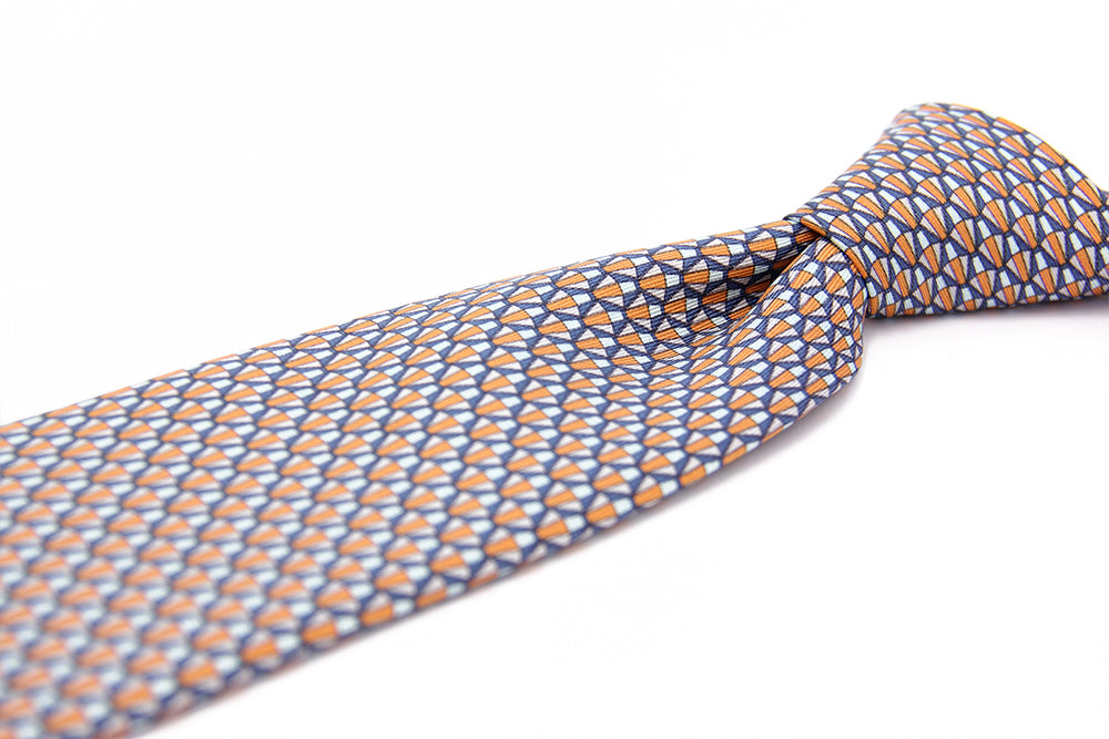 A silk tie with a geometric pattern in orange and white colors, displayed on a white background.