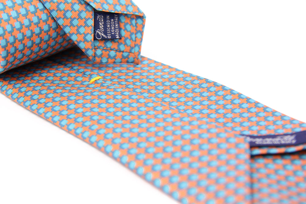 A patterned silk tie with a combination of peach and blue colors, displayed in a folded and unfolded configuration.