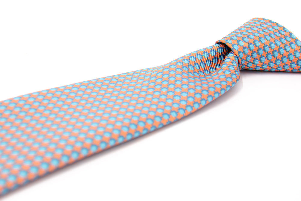 A patterned silk tie with a combination of peach and blue colors, displayed in a folded and unfolded configuration.