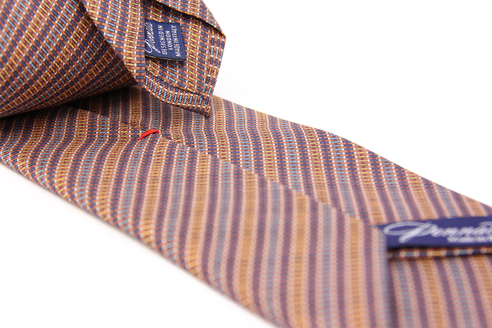 A silk tie with a geometric pattern in orange and white colors, displayed on a white background.
