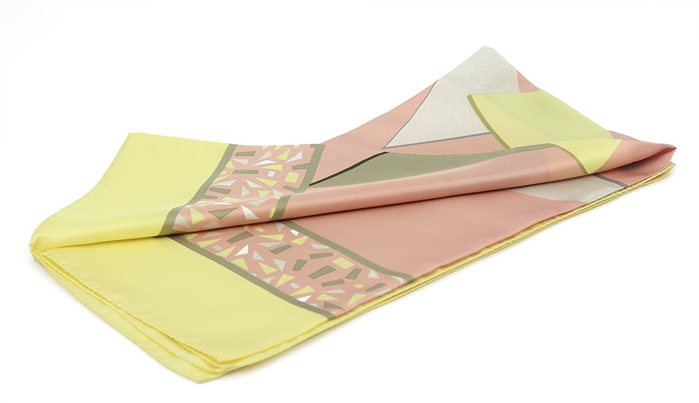 A folded silk pocket square with a geometric pattern featuring yellow, pink, green, and other colors.