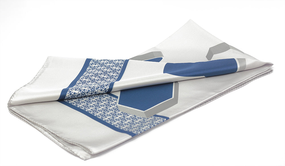 A folded silk pocket square with a geometric pattern in silver and blue colors.