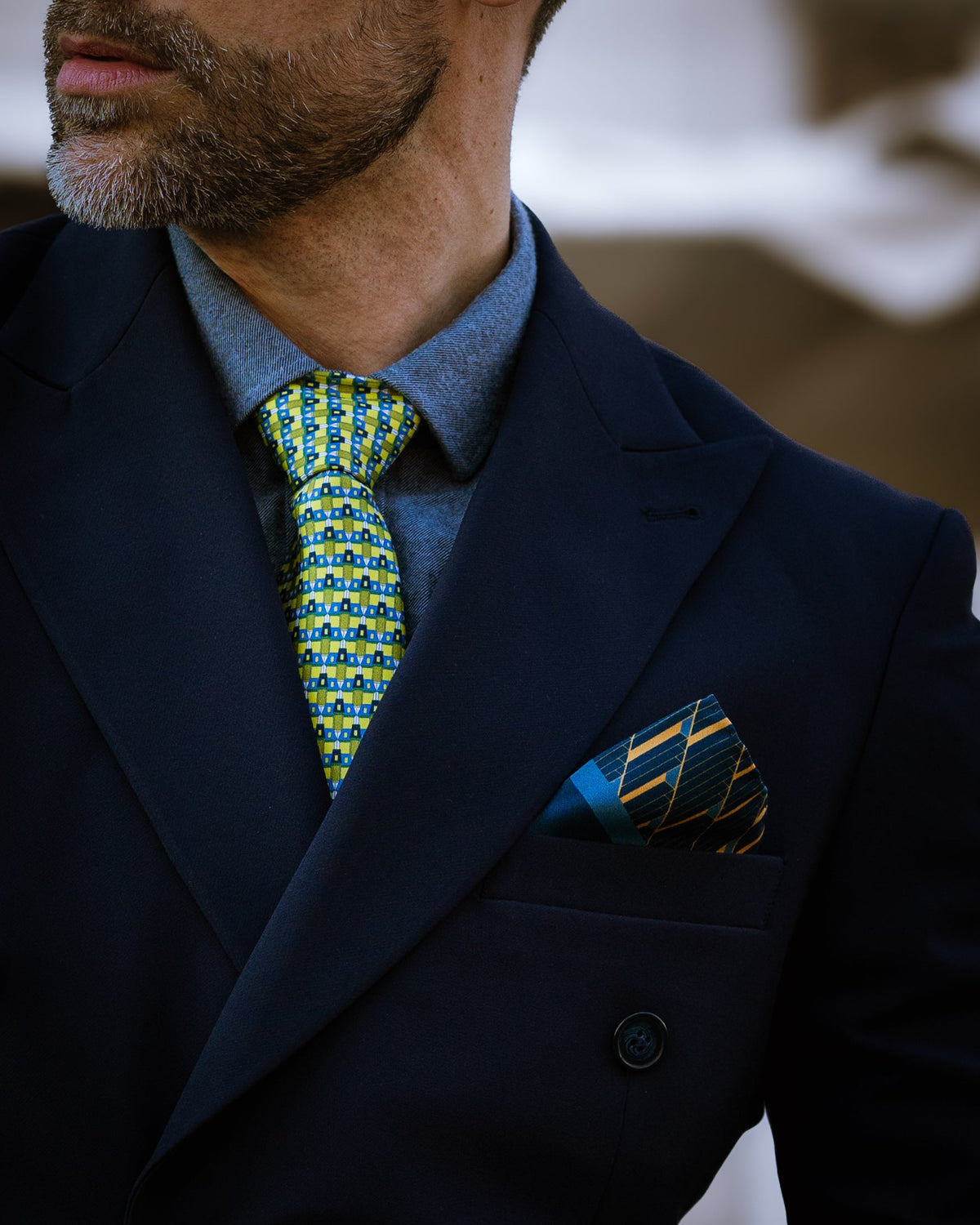 Man wearing a dark suit with a blue shirt, patterned designers silk tie, and matching pocket square.