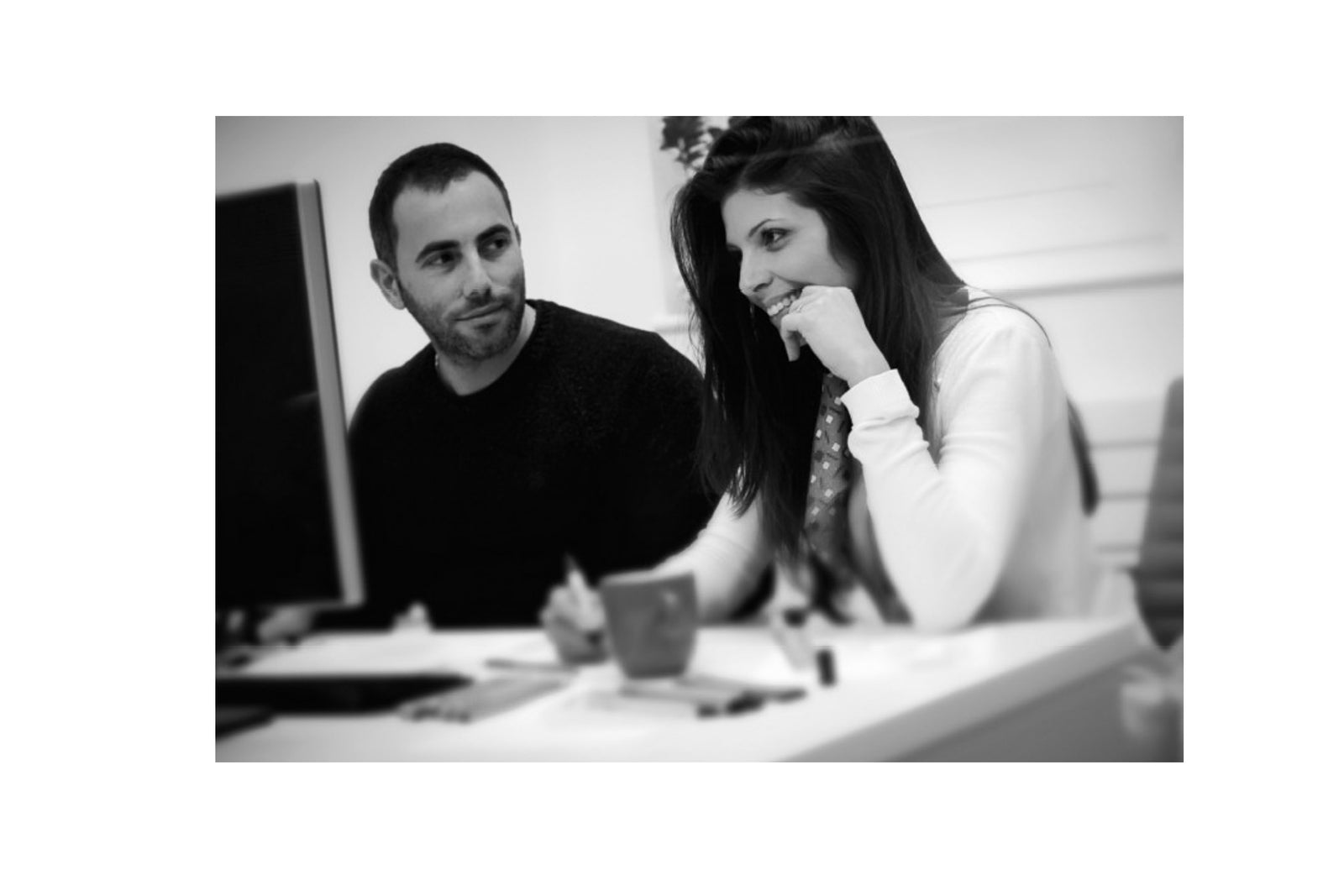 Two people sitting at a desk with a computer screen in the background