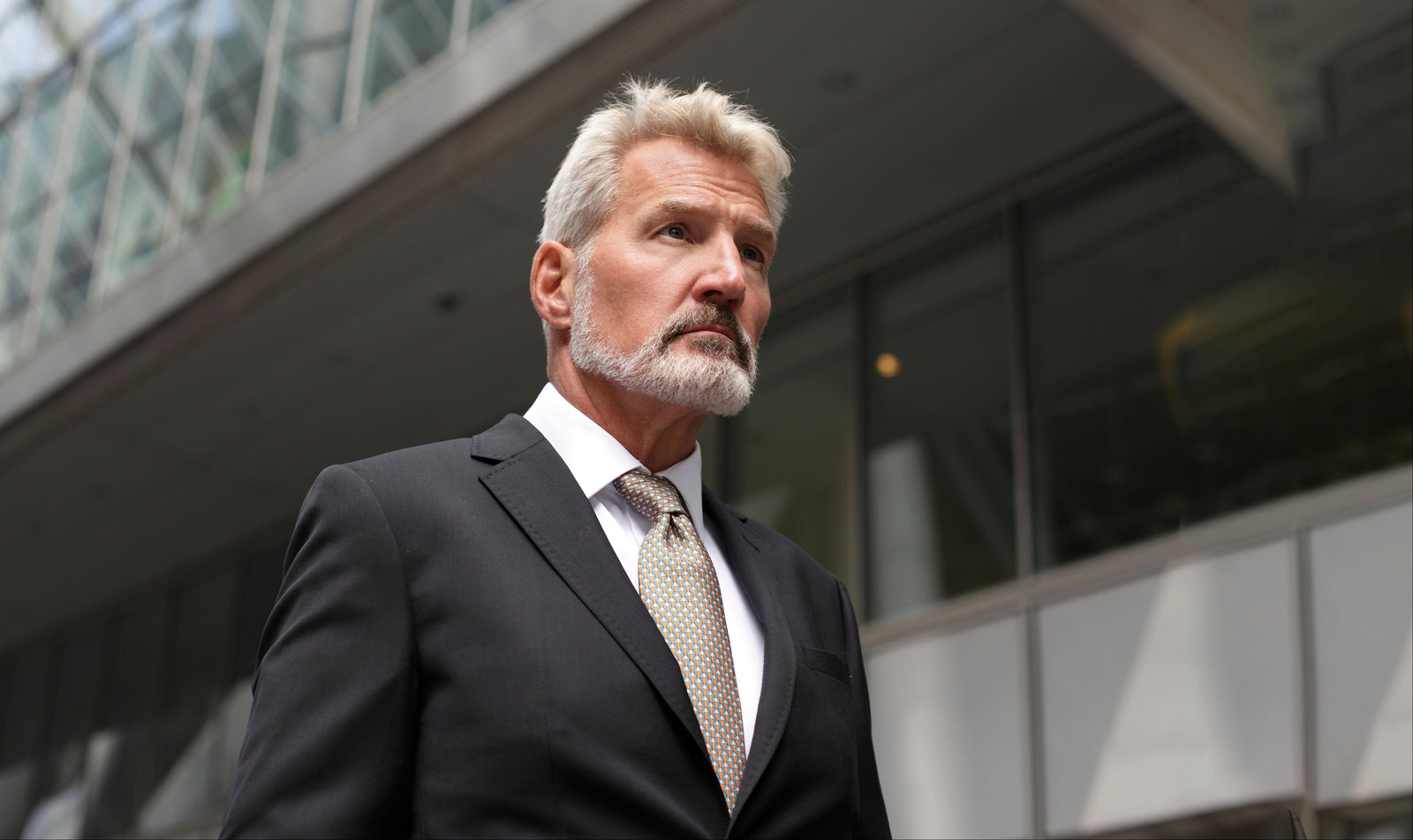 Man in a black suit standing outside a modern building, with a silk designers tie