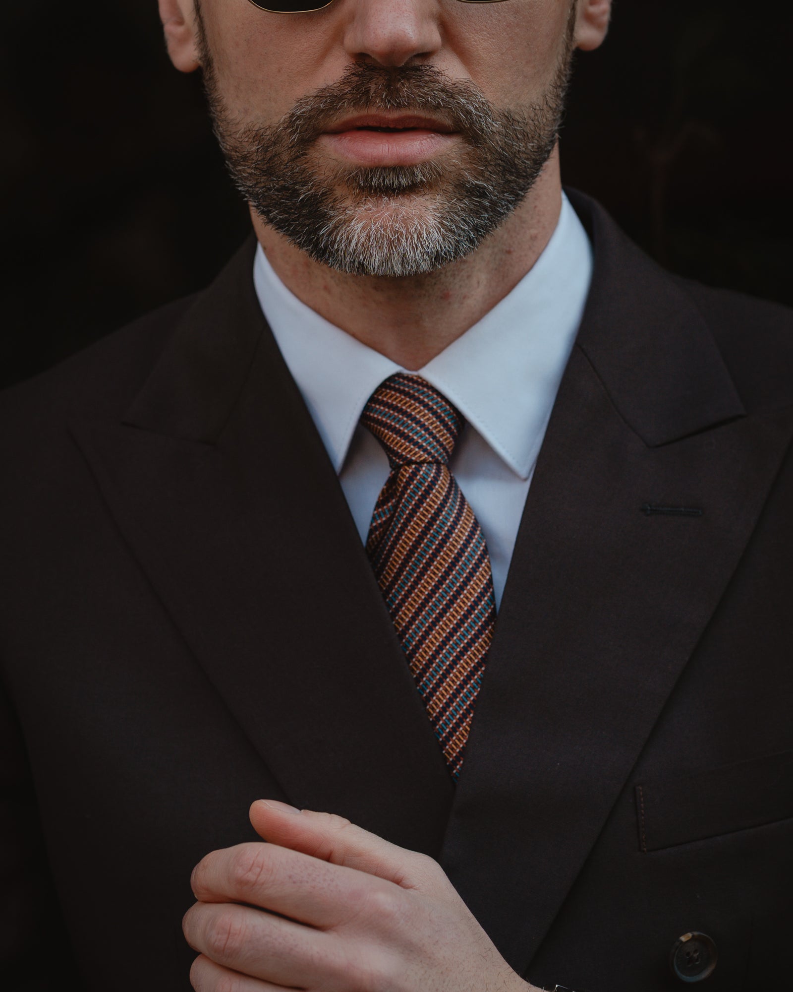 Man wearing a dark suit and striped tie with a blurred background